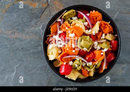 Colorato tortellini con insalata di pomodoro e cipolle, vista aerea al buio su un sfondo di ardesia Foto Stock