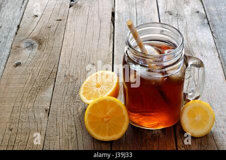 Mason vasetto in vetro freddo di tè freddo con fette di limone su un rustico sfondo legno Foto Stock