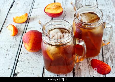 Due mason jar bicchieri di pesca artigianale tè freddo su un rustico di legno bianco sullo sfondo Foto Stock