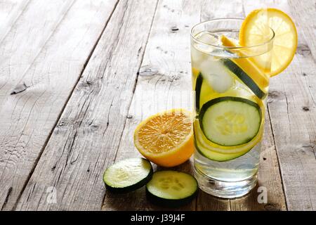 Limone cetriolo detox di acqua in un bicchiere con fettine contro un rustico sfondo legno Foto Stock