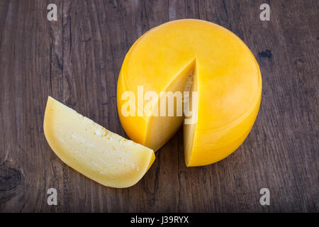 Testa di formaggio con una fetta tagliata sul tavolo di legno Foto Stock