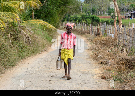 Un tribale uomo Tamil indossando abiti tradizionali passeggiate lungo una strada di campagna in un villaggio rurale in Tamil Nadu, India meridionale, Asia del Sud Foto Stock