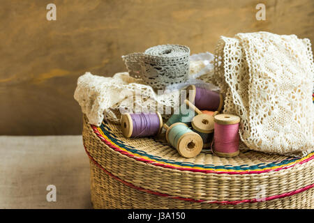 Tessuti artigianali di rattan e la cucitura di alimentazione scatola in legno, bobine, rotoli di pizzo, invecchiato Sfondo legno, hobby fashion concept, close up Foto Stock