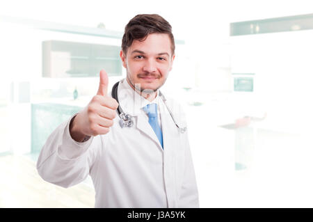 Felice medico o medico in camice bianco dando un pollice in alto con la mano destra Foto Stock