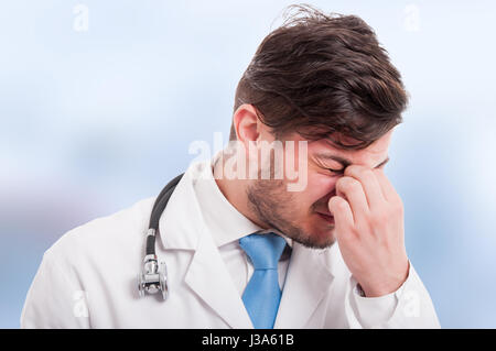 Primo piano di giovani stanchi medic con mal di testa dopo una lunga giornata isolato su sfondo blu Foto Stock