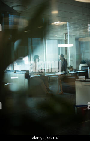 La gente di affari che interagiscono con ogni altro durante la riunione in ufficio visto attraverso il vetro Foto Stock