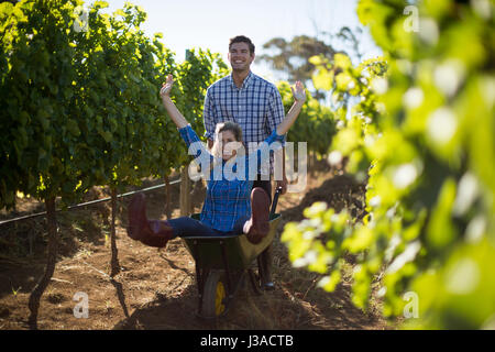 L'uomo spingendo il suo allegro fidanzata in carriola in vigna durante la giornata di sole Foto Stock