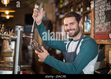 Ritratto di barman versare birra dal rubinetto in vetro al bar Foto Stock