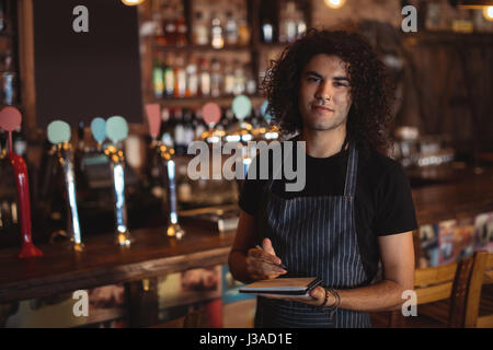 Ritratto di giovane cameriere scrivendo sul diario in pub Foto Stock