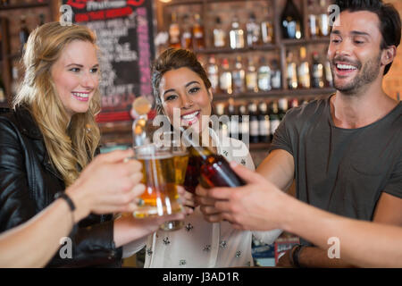 Allegro amici tostare boccali da birra e bottiglie in bar Foto Stock
