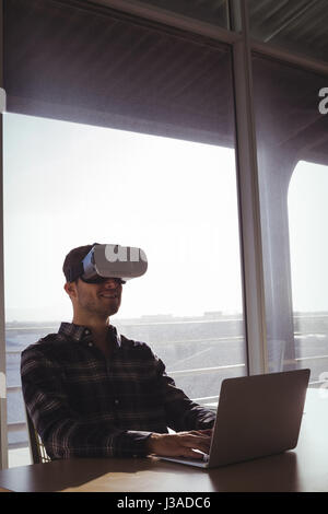 Giovane imprenditore indossando la realtà virtuale cuffie mentre utilizzando computer portatile in ufficio Foto Stock