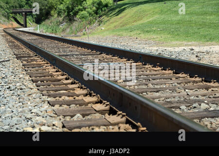 Il treno via andando attorno a piegare e sotto il ponte in background Foto Stock