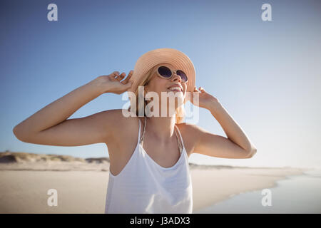 Donna felice di indossare occhiali da sole e cappello in spiaggia durante il giorno di sole Foto Stock