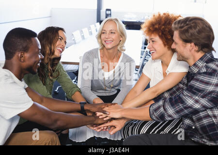 Sorridente la gente di affari mani di impilamento seduti su sedie in ufficio Foto Stock