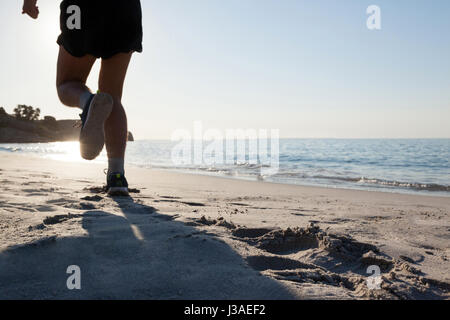 Vista posteriore dell'uomo jogging sulla spiaggia contro il cielo blu Foto Stock