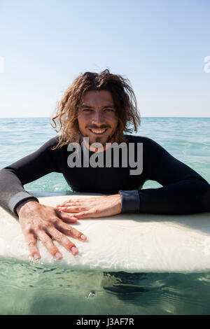 Ritratto di sorridere surfer appoggiata sulla tavola da surf in mare Foto Stock