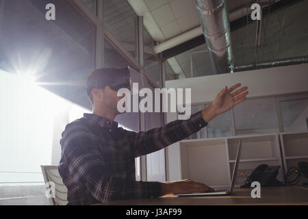 Giovane imprenditore gesticolando mentre utilizzando la realtà virtuale auricolare in ufficio il giorno di sole Foto Stock