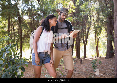 Coppia giovane con tavoletta digitale mentre in piedi nella foresta Foto Stock