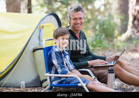 Ritratto di sorridere padre e figlio con il computer portatile nella foresta Foto Stock