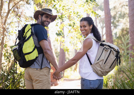 Vista posteriore del ritratto di Giovane escursionismo coppia tenendo le mani nella foresta Foto Stock