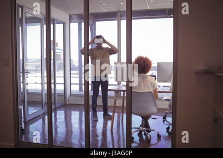 Femmina collega di lavoro mentre il proprietario indossa le cuffie VR in office Foto Stock