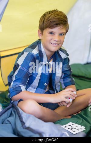 Ritratto di di sorridere ragazzo giocando a carte mentre è seduto in tenda Foto Stock