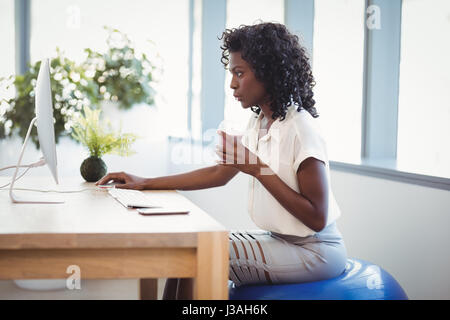 Executive seduti sulla sfera di fitness mentre si lavora alla scrivania in ufficio Foto Stock