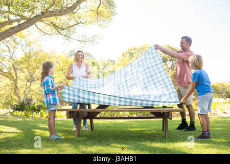 Famiglia di diffondere la tovaglia sul tavolo da picnic nel parco Foto Stock