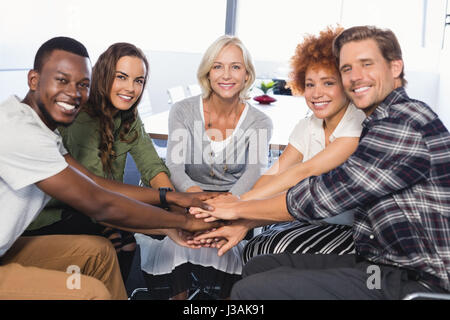 Ritratto di sorridere la gente di affari mani di impilamento seduti su sedie in ufficio Foto Stock