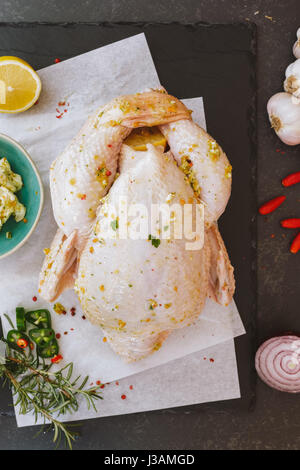 Tutto il pollo crudo sulla carta da forno con il condimento prima della cottura vista superiore vintage tonica immagine spazio di copia Foto Stock
