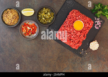 Tartare di manzo con un tuorlo d'uovo e gli altri ingredienti sul rustico sfondo testurizzata vista dall'alto, uno spazio vuoto Foto Stock
