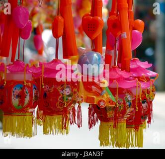 Close up rosa luminoso,rosso e giallo a buon mercato dei giocattoli di plastica con il cartoon-tipo figure e frange appesa in un negozio display Foto Stock