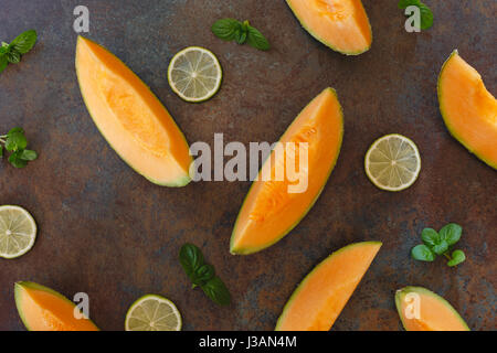 Fette di melone Cantalupo e calce rustico sfondo scuro. Vista superiore, copia dello spazio, laici piatta Foto Stock