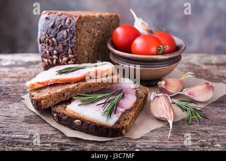 Tradizionali ucraine sandwich fatti di marrone pane di segale e lardo affumicato su un pezzo di carta marrone e legno naturale superficie testurizzata con unfocused Foto Stock