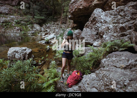 Escursionista femmina avente il caffè sulla roccia nella foresta Foto Stock