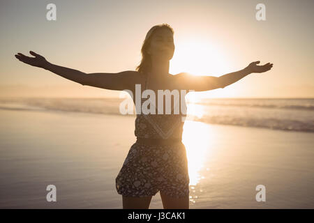 Giovane donna con le braccia aperte in piedi in spiaggia durante il tramonto Foto Stock
