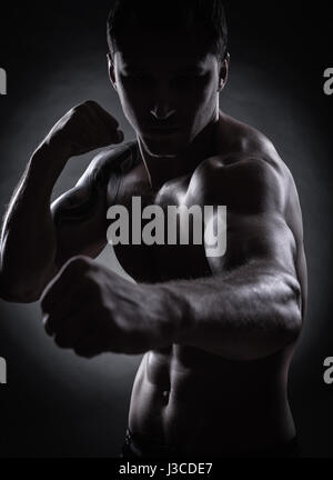 Fighter silhouette. Bello athletic uomo nella boxe stand su sfondo scuro Foto Stock