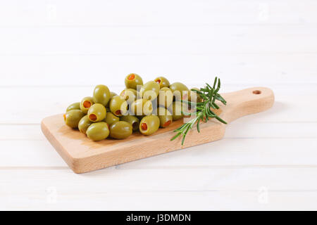 Pila di olive verdi ripiene di peperone rosso sul tagliere di legno Foto Stock