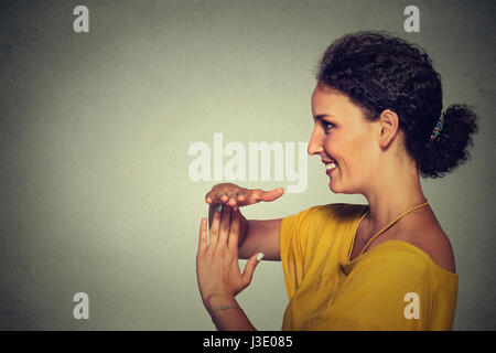 Profilo laterale verticale, giovani, felice, donna sorridente che indica il tempo fuori gesti con le mani isolato muro grigio Sfondo. Positivo emozione umana ex facciale Foto Stock