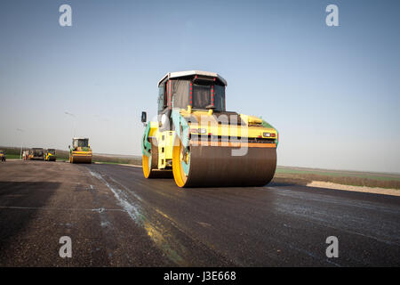 Compattatore di asfalto accumulano un nuovo strato di asfalto su una nuova strada asfaltata in costruzione Foto Stock