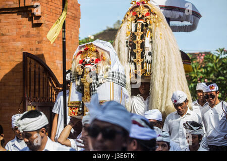 Uomini mascherati in scary Rangda costumi il demone regina delle streghe sono portati in una cerimonia di Bali circondato da orde di Balinese devoti indù Foto Stock