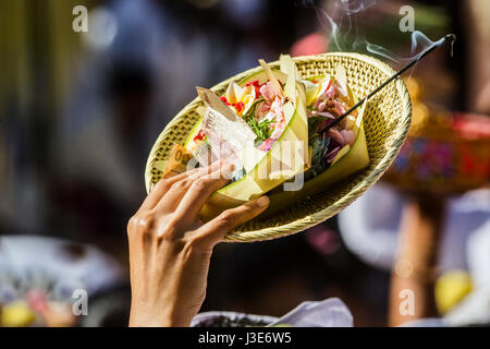 Canang Balinese Sari religiosi offerte e incenso essendo portato da un devoto indù oggetto tenuta alta sopra la folla ad una cerimonia religiosa Foto Stock