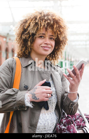 La donna in attesa presso la stazione ferroviaria per il suo treno. Ella è con il suo smart phone per controllare i tempi. Foto Stock