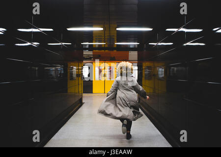 Vista posteriore di imprenditrice correre per prendere il treno della metropolitana, che è già in partenza dalla stazione della metropolitana. Foto Stock