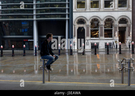 Un 19-anno vecchio adolescente siede sulla stazione di ringhiere durante la primavera di precipitazioni su Cannon Street, 1 maggio 2017, nella città di Londra, Inghilterra. Foto Stock