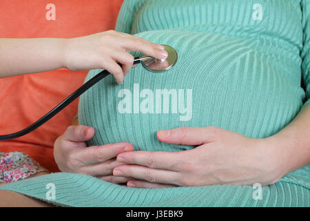 Figlia medico utilizzando uno stetoscopio esaminando bianco donna incinta. Foto Stock