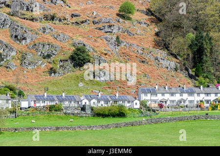 Pannelli solari su una fila di case e bungalow ai piedi di una collina (caduto) in una giornata di sole in primavera a Chapel Stile, Lake District, Cumbria, Engl Foto Stock