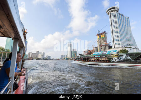 Donna su un Chao Phraya Express barca guardando un altra barca e grattacieli lungo il Fiume Chao Phraya a Bangkok, in Thailandia. Foto Stock