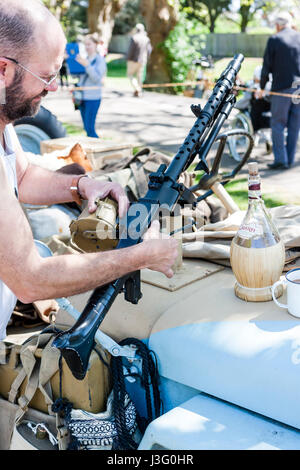 Saluto alla 40's rievocazione evento. Deserto area di ratti, uomo di regolazione e ingrassaggio macchina tedesca pistola sul cofano della jeep. Foto Stock