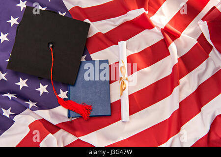 Vista superiore del libro, graduazione mortarboard e diploma a noi bandiera sfondo, il concetto di istruzione Foto Stock